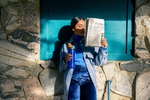 Person reading a newspaper and holding an Owala bottle to stay hydrated