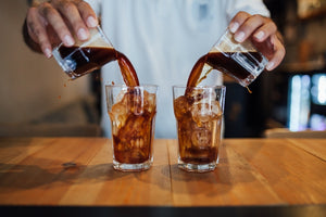 Barista pouring freshly brewed coffee into two cups, with steam rising from the rich brew.